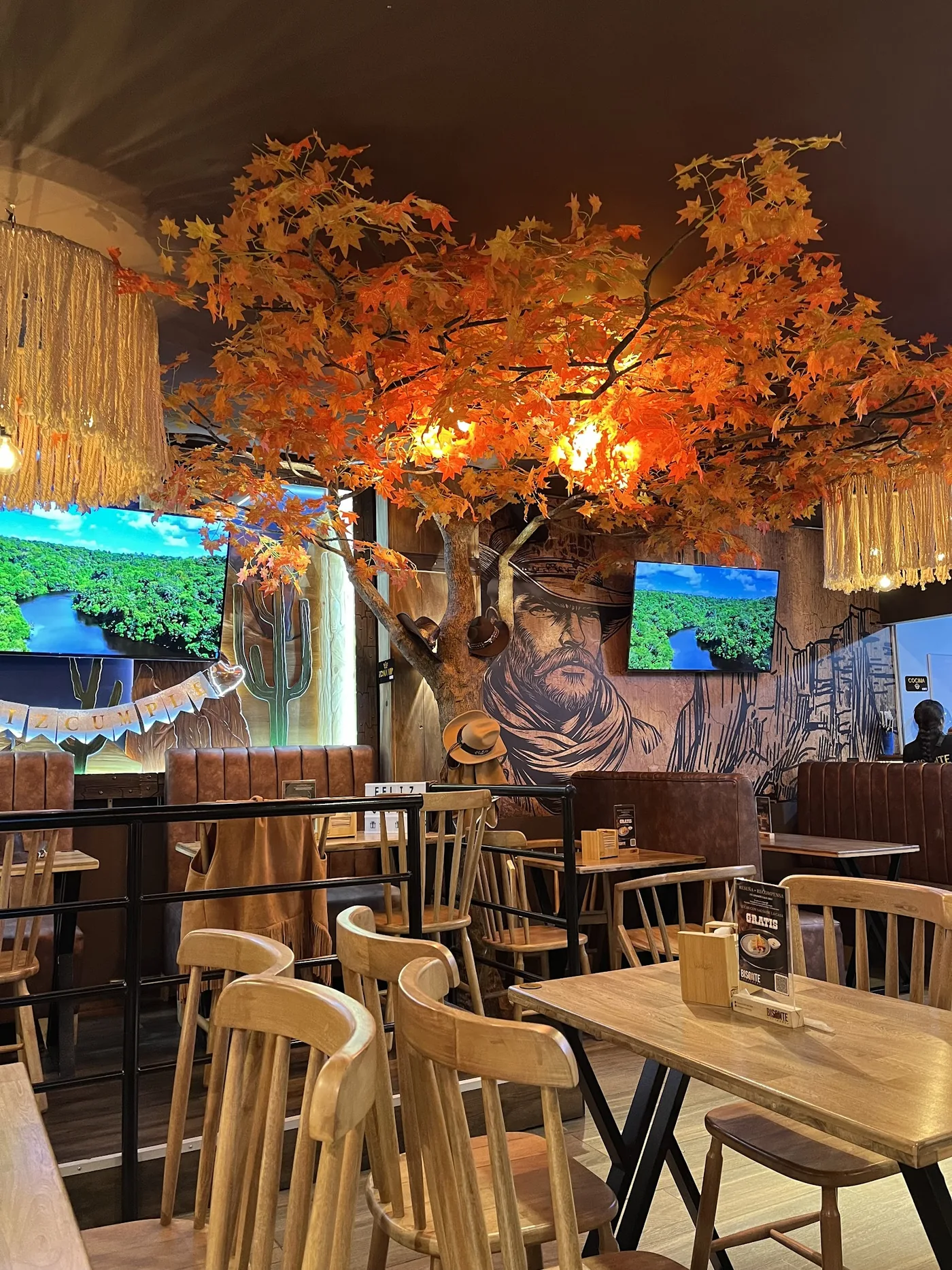 Salón de Bisonte Gastrobar con árbol otoñal iluminado y mural del vaquero